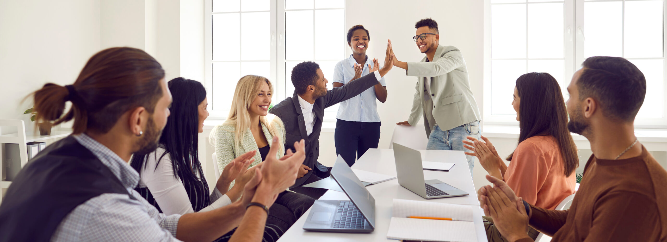 Happy young man gives high five to colleague while diverse business team is applauding